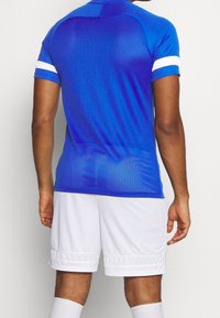 Blue athletic jersey with short sleeves and white stripes at the cuffs, paired with white shorts, featuring a fitted design and textured fabric.