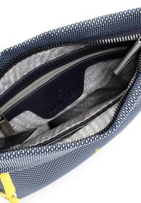 Interno di una borsa in tessuto intrecciato navy che mostra una fodera grigia con testo stampato, scomparti con zip e una tracolla di accento gialla. Visibili dettagli in metallo argentato.