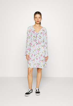 Vestido estampado floral em tecido azul claro com mangas longas e um laço no decote, combinado com ténis pretos.