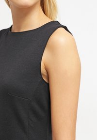 Czarny bezrękawnik z okrągłym dekoltem i subtelną boczną kieszenią, wykonany z gładkiego, elastycznego materiału o dopasowanej sylwetce.