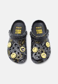 Crocs noirs présentant un motif de différents emojis souriants. Fabriqués en matériau léger avec des trous de ventilation et une sangle noire.