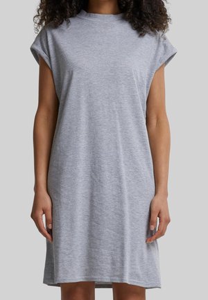 Vrouw draagt een mouwloze, lichtgrijze, knielange casual jurk tegen een effen achtergrond.