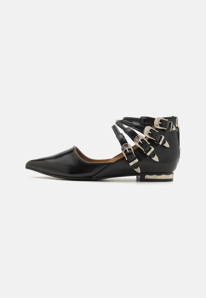 Chaussure plate en cuir verni noir avec un bout pointu, des brides autour de la cheville et des boucles en métal argenté. Elle présente un petit talon avec des accents texturés.