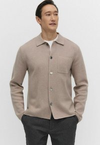 Lichtbeige cardigan van zachte stof, met een spitse kraag, knopen aan de voorkant en een enkele borstzak. Effen kleur, minimalistisch ontwerp.