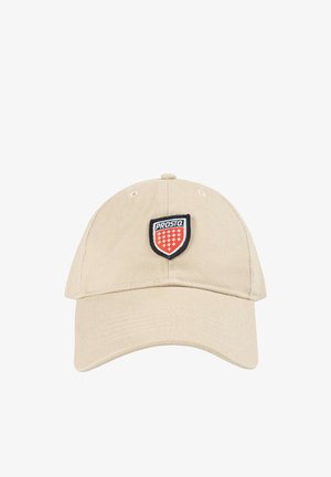 Beżowa czapka bejsbolowa z zakrzywionym daszkiem i naszywką w kształcie tarczy z napisem „PROSTO” nad czerwonymi i białymi symbolami krzyża.