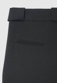 Pantalon noir sur mesure avec une texture lisse, présentant une ceinture plissée et une seule poche arrière sans quincaillerie visible.