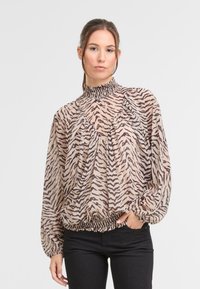 Lekka, przezroczysta bluzka z wysokim, falbaniastym kołnierzem i luźnym, drapowanym krojem. Posiada beżowe tło z brązowymi paskami przypominającymi zebry.