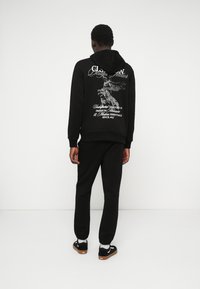 Moletom preto com estampado gráfico nas costas, combinado com calças de moletão pretas e sapatilhas pretas. Tecido suave, corte relaxado, punhos canelados.