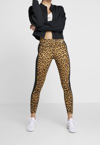 Legginsy w cętki z czarnym bokiem, wykonane z elastycznego materiału, w połączeniu z krótką czarną kurtką na zamek i białymi trampkami.
