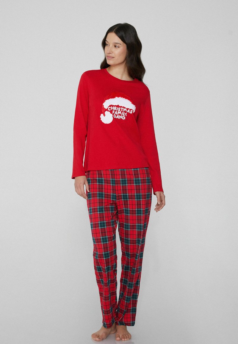 Rode top met lange mouwen met een witte afbeelding van een kerstmanmuts en de tekst "Christmas Family Gang". Gecombineerd met rood-groen geruite pyjamabroek.