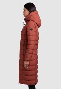 Lange, puffy jas in roestkleur met een capuchon, voorzien van horizontale stiksels, zijzakken en een zwarte accentknop.