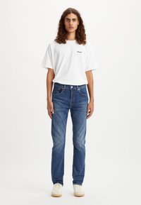 Biela bavlnená tričko s logom "Levi's", v kombinácii s modrými denimovými džínsy so rovnými nohavicami, s detailmi blednutia a bielymi teniskami.