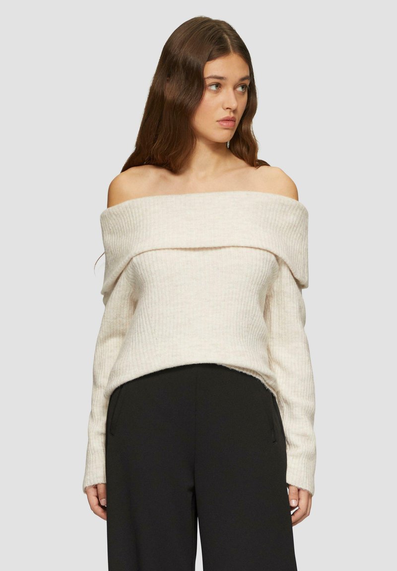 Crèmekleurige ribgebreide trui met off-the-shoulder mouwen, lange mouwen en een cropped zoom, gecombineerd met zwarte hooggewaagde broeken.