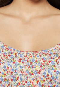 Tessuto a motivo floreale con piccoli fiori rossi, blu e gialli su uno sfondo chiaro; caratterizzato da una texture arricciata e scollatura a barchetta.