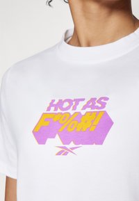 T-shirt bianca in cotone con un audace design grafico testuale multicolore in viola e giallo, caratterizzato da un font moderno e dettagli del logo.