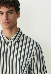 Polo a rayas con rayas verticales en azul marino y crema, hecho de un tejido texturizado con cuello abotonado y mangas cortas.