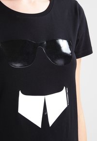 Camiseta negra con un gráfico de gafas de sol negras brillantes y un cuello blanco impresos en el pecho.