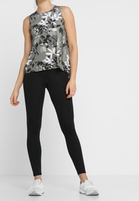 Szary, kwiecisty top bez rękawów z białymi i czarnymi akcentami. W połączeniu z czarnymi legginsami i białymi sportowymi butami. Gładka tkanina, casualowy design.