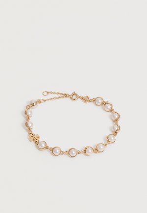 Bracelet chaîne en or avec des perles blanches rondes espacées régulièrement et un petit fermoir circulaire sur fond blanc.