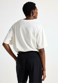 Cremefarvet bomulds t-shirt med korte ærmer, afslappet pasform og rund hals. Sammen med sorte bukser med sidelommer.