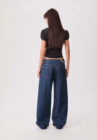 Wijde denim broek in donkerblauw, met een hoge taille, twee achterzakken en stikdetails. Gecombineerd met een nauwsluitend zwart topje.