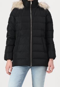 Zwarte donsjas met ritssluiting, capuchon met bontvoering, geribbelde mouwboorden en twee steekzakken aan de voorkant. Gewatteerd ontwerp met een lichtgewicht textuur.