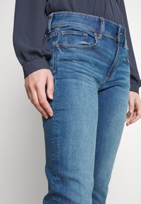 Blå denimjeans med slim fit, femficksdesign och subtila blekningar. Midjebandet har bältesöglor och kontrasterande sömdetaljer.