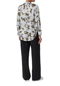 Camicia a maniche lunghe di colore verde oliva con grande motivo floreale azzurro chiaro, orlo arrotondato e polsini abbottonati, abbinata a pantaloni larghi neri.