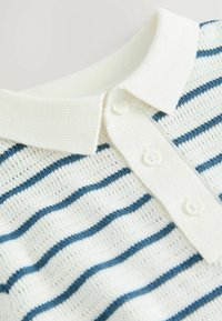 Randig pikétröja med en krämfärgad bas och blå ränder, med ett strukturerat tyg, knappslå och en ribbad krage.
