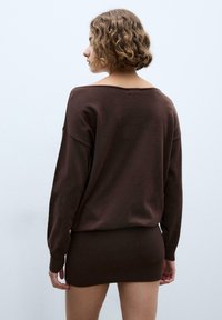 Ensemble pull brun tricoté et mini-jupe, présentant une coupe ample, une texture côtelée et un col large, mettant en valeur une couleur marron foncé unie.