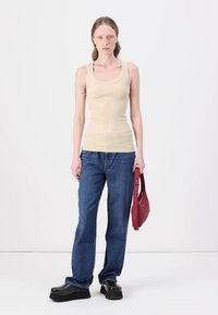 Beige ribbenpaita, siniset løse jeans, sorte platåsko og en liten rød håndveske. Enkel design uten synlige mønstre.