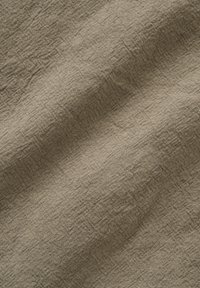 Tissu beige tissé avec texture visible et plis diagonaux subtils créant des variations de lumière et d'ombre sur la surface.