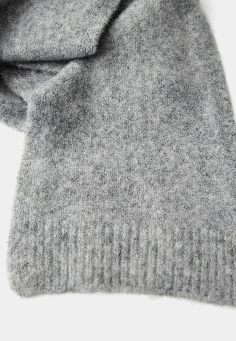 Étole grise en laine douce, pliée et avec des bords côtelés, présentée sur un fond blanc.