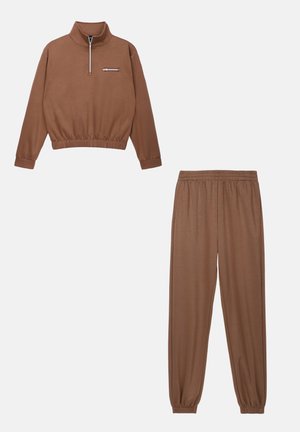 Bruin sportoutfit met een pullover met rits en een opstaande kraag, en elastiche taillebroek, beide gemaakt van een zachte, gladde stof met ribgebreide boorden.