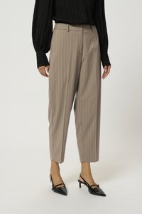 Pantalon beige à rayures avec une coupe droite, présentant une texture lisse et des passants de ceinture, associé à des talons aiguilles noirs.