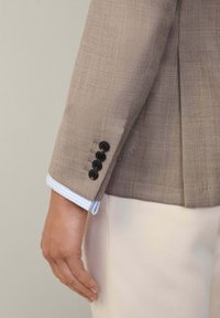 Manche en lin beige d'un blazer avec cinq boutons foncés, exposant un poignet de chemise à carreaux vichy bleu clair et blanc en dessous.