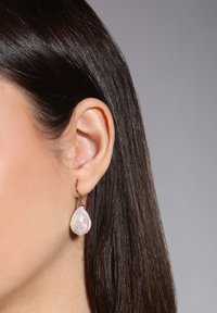 Goldene Creolen mit einer tropfenförmigen, schimmernden Perle. Der Ohrring wird ins Ohr eingehakt und zeichnet sich durch elegante, glatte Texturen aus.