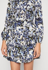 Mekko pitkillä hihoilla, jossa on monivärinen abstrakti kuvio sinisen, vihreän ja valkoisen sävyissä. Varustettu vyötärösoljella ja taskuilla.