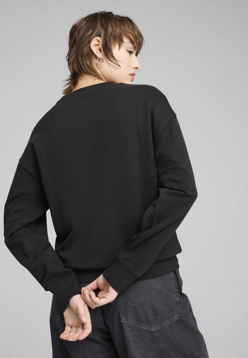 Schwarzer Pullover mit lässiger Passform, überschnittenen Schultern und gerippten Bündchen. Kombiniert mit dunkelgrauen Cargo-Hosen, ohne sichtbare Muster oder Akzente.