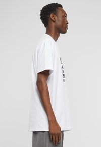 T-shirt en coton blanc à manches courtes et à coupe décontractée, avec un motif graphique noir à l'avant. Texture douce, col rond standard.