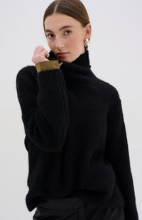 Maglioncino nero lavorato a maglia con colletto alto, caratterizzato da un motivo testurizzato e accenti color beige nei polsini. Tessuto morbido con una vestibilità comoda.