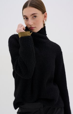 Black knitted sweater with a high collar, featuring a textured pattern and tan cuff accents. Soft fabric with a relaxed fit.