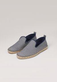 Chaussures à enfiler de style espadrille avec un motif à carreaux bleu marine et blanc. Tige en tissu avec semelle en corde de jute, doublure bleu foncé et deux languettes de tirage.