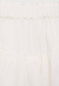White, lightweight fabric with a subtle texture. Features a gathered elastic waistband and a tiered ruffle detail at the hem.