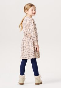 Blomsterprydd klänning i mjuk rosa med puffärmar och elastisk midja, kombinerad med randiga marinblå leggings och beige stövlar fodrade med fuskpäls.