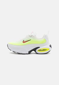 Vita Nike sneakers med en neon gul och svart sula, som har en strukturerad ovandel, en framträdande Air-enhet och en röd logotypaccent.