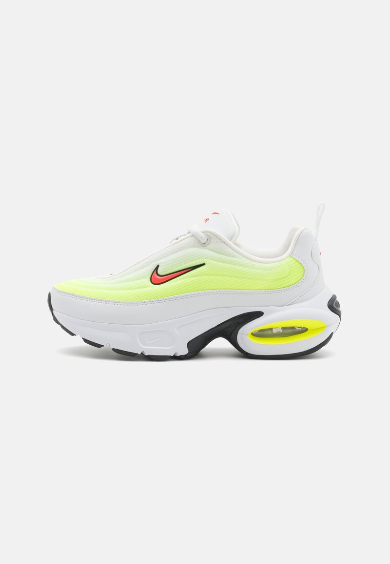 Vita Nike sneakers med en neon gul och svart sula, som har en strukturerad ovandel, en framträdande Air-enhet och en röd logotypaccent.