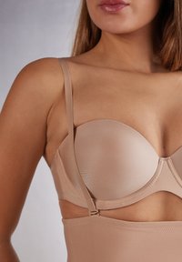 Beige bh met voorgevormde cups en verstelbare bandjes. Gladde textuur met een subtiele glans, voorzien van een naadloos ontwerp en haaksluiting.