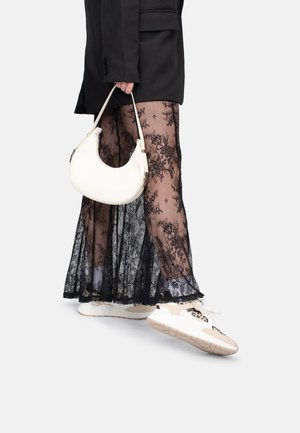 Black lace skirt layered over sheer fabric, paired with white handbag and multi-colored sneakers. The outfit includes a black blazer.