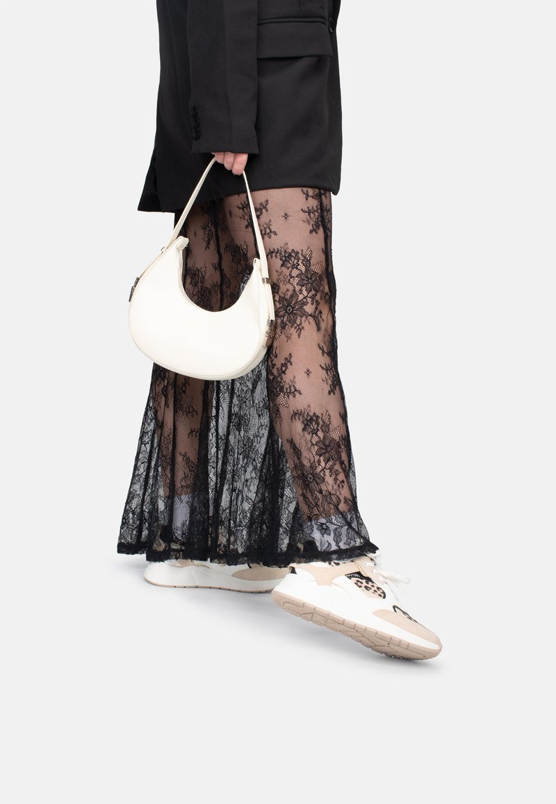 Schwarzer Spitzenrock, der über transparentem Stoff geschichtet ist, kombiniert mit einer weißen Handtasche und mehrfarbigen Sneakers. Das Outfit beinhaltet ein schwarzes Blazer.